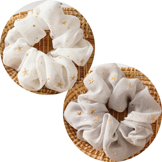 White scrunchies with gold stars on a woven surface