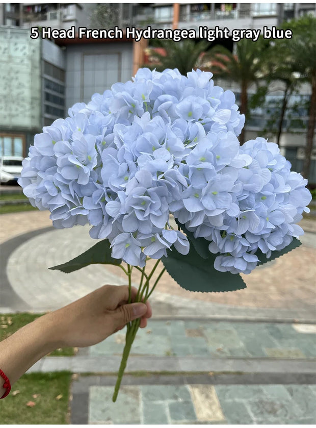 Bouquet of light gray blue French hydrangea held by a person outdoors.