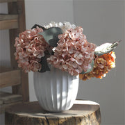 White vase with pink and orange flowers on a wooden surface