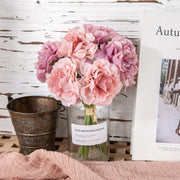 Bouquet of pink flowers in a glass vase on a wooden surface with a rustic background.