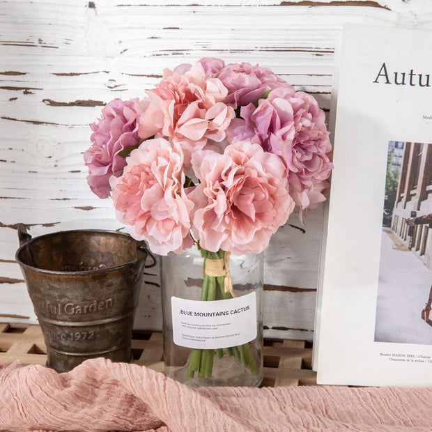 Bouquet of pink flowers in a glass vase on a wooden surface with a rustic background.