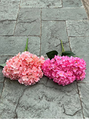 Two pink artificial hydrangea flowers on a stone pavement.