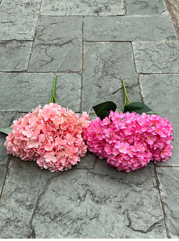 Two pink artificial hydrangea flowers on a stone pavement.