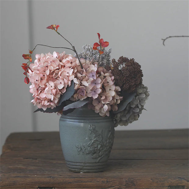 Decorative vase with flowers on a wooden surface against a plain background