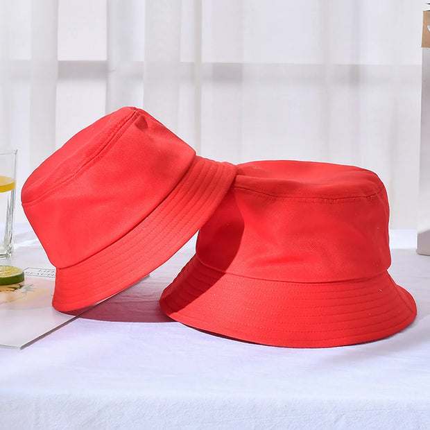 Two red bucket hats on a white surface with a light curtain background