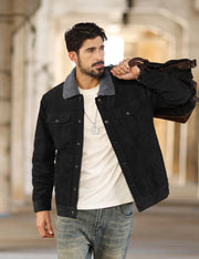Man wearing a black jacket with a gray collar, white shirt, and jeans, holding a brown leather bag.
