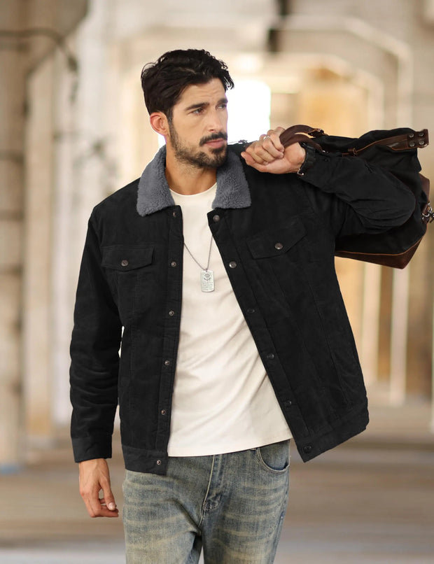 Man wearing a black jacket with a gray collar, white shirt, and jeans, holding a brown leather bag.