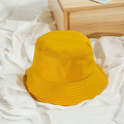 Yellow bucket hat on a white fabric surface with a wooden surface in the background