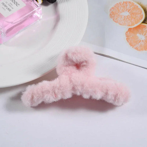 Pink fluffy heart-shaped object on a white surface with a pink perfume bottle in the background.