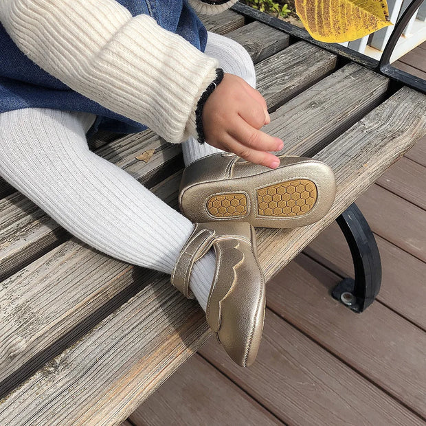 Person sitting on a wooden bench wearing gold shoes with yellow soles.