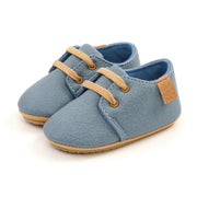 Pair of blue baby shoes with brown laces and sole on a white background