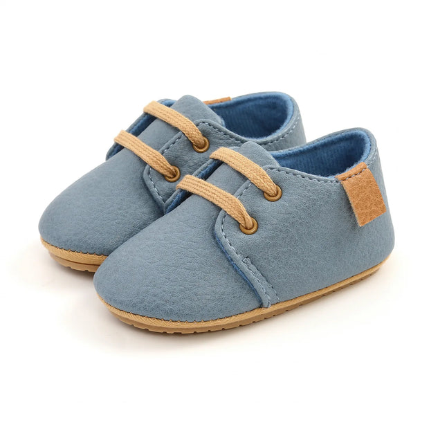 Pair of blue baby shoes with brown laces and sole on a white background