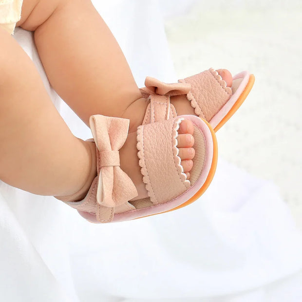 Close-up of a child's foot wearing a pink sandal with a bow on a white background