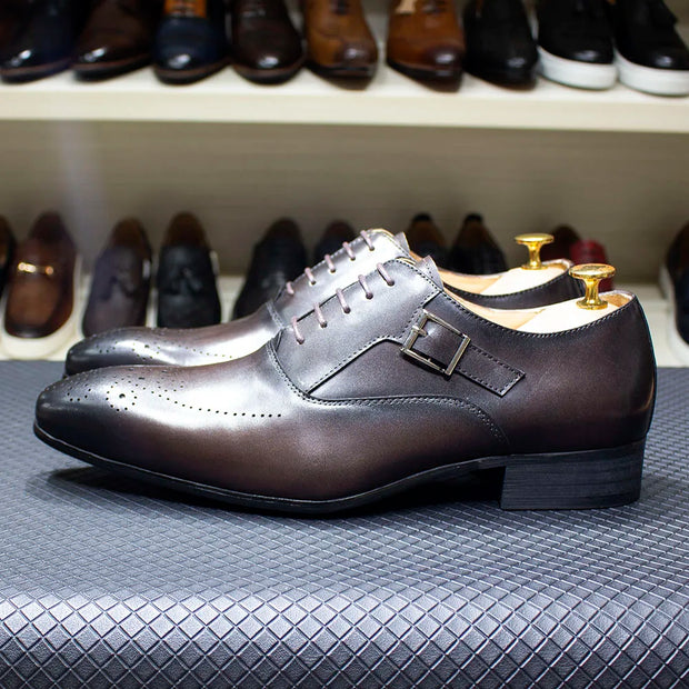 Pair of brown dress shoes with gold buckles on a textured surface, with a shelf of other shoes in the background.