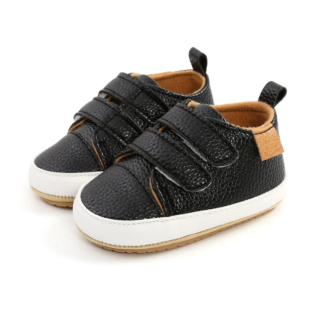 Pair of black children's shoes with brown accents on a white background