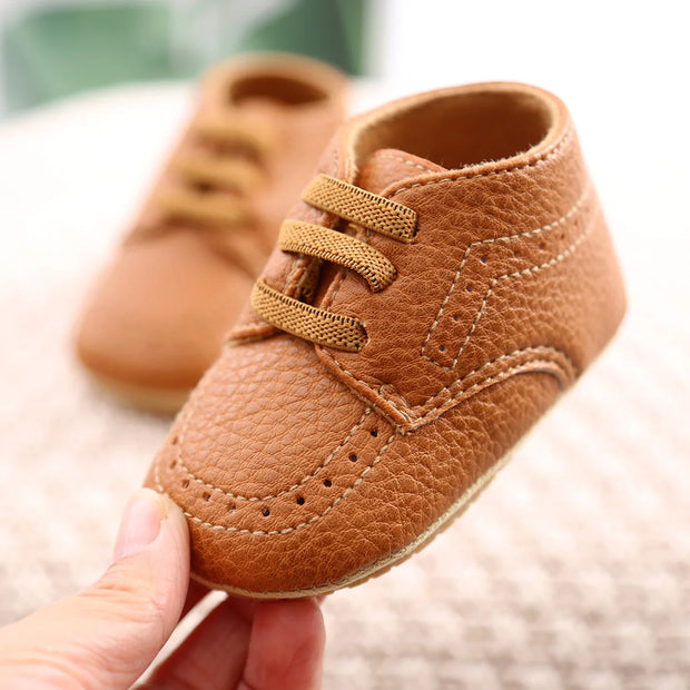 Brown leather baby shoes held by a hand with a blurred background