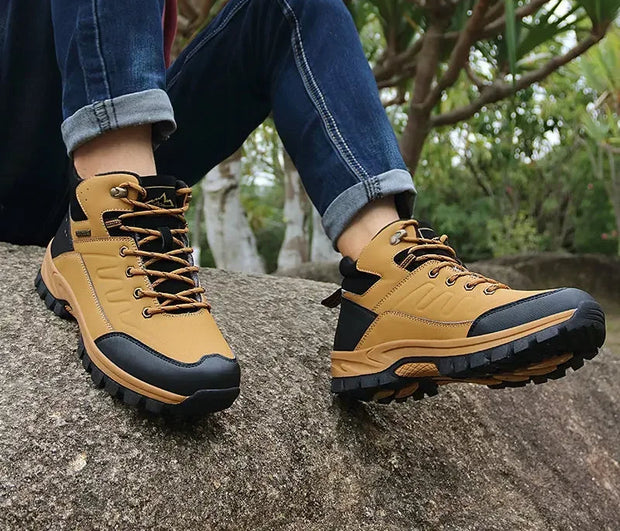 Person wearing tan hiking boots with black soles on a rock, with a blurred natural background.