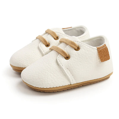 White baby shoes with brown accents on a white background