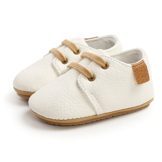 White baby shoes with brown accents on a white background