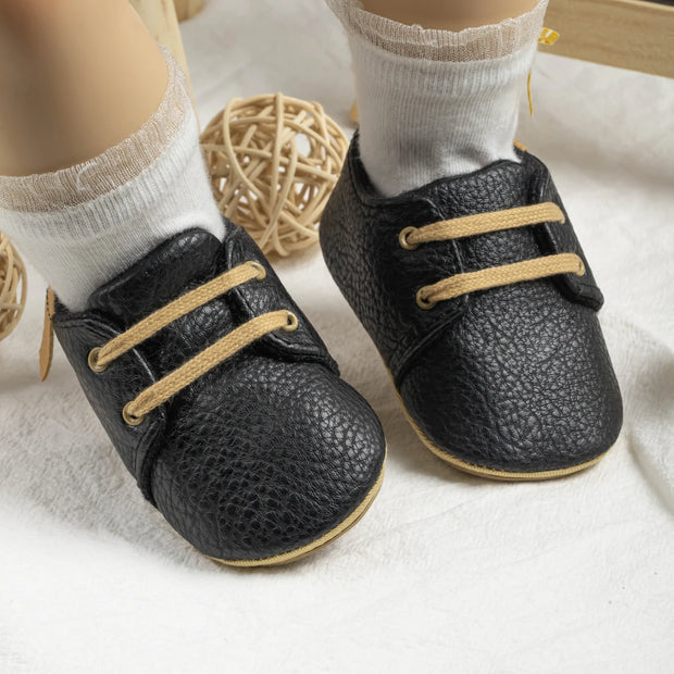 Black baby shoes with tan laces worn by a child on a light background