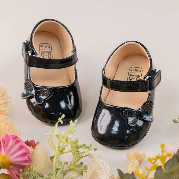 Black patent leather shoes with bows on a light background with flowers.