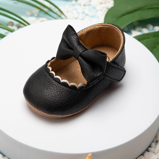 Black leather baby shoe with a bow on a white surface