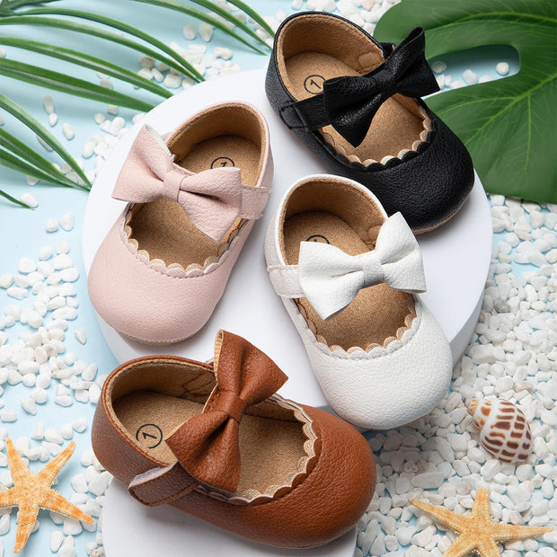 Set of children's shoes with bows on a pebble surface with starfish and shells.