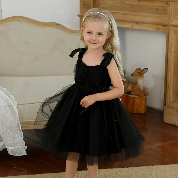 Young girl in a black dress standing in a room with wooden furniture and a deer figurine.