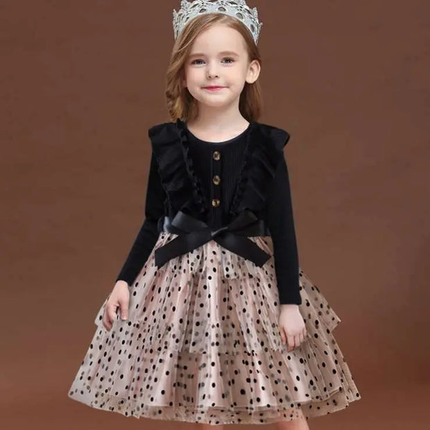 Young girl wearing a black cardigan over a polka dot dress with a tiara on a brown background