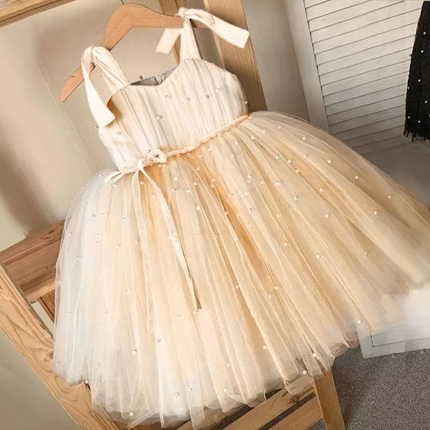 Beige tulle dress with a belt on a wooden hanger against a neutral background
