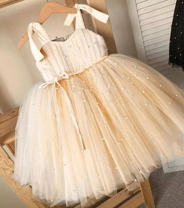 Beige tulle dress with pearl embellishments on a wooden hanger.