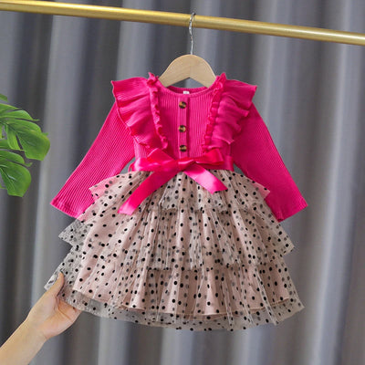 Children's outfit with pink top and polka dot skirt on a hanger against a gray curtain background.