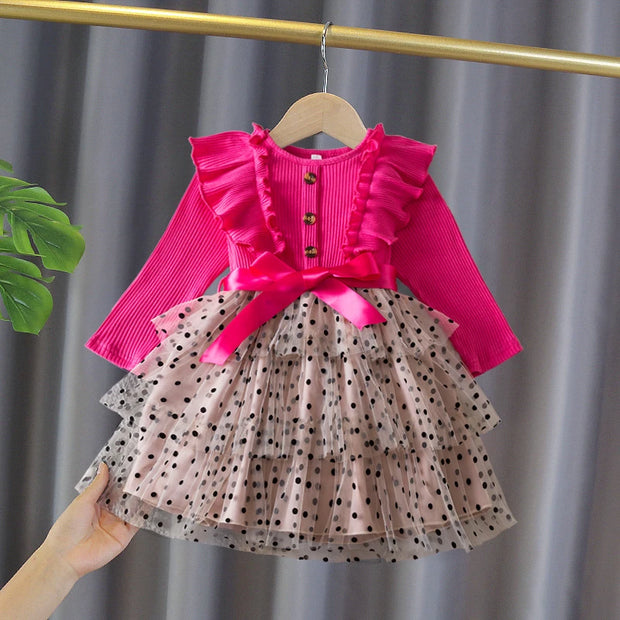 Children's outfit with pink top and polka dot skirt on a hanger against a gray curtain background.