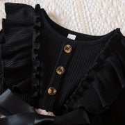Black ribbed top with ruffled details and buttons on a textured surface