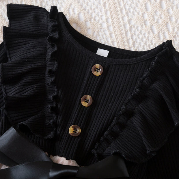 Black ribbed top with ruffled details and buttons on a textured surface