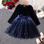 Navy blue dress with a bow on a hanger, surrounded by flowers and shoes on a textured surface.