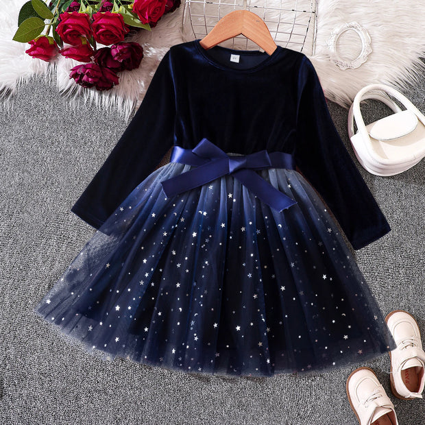 Navy blue dress with a bow on a hanger, surrounded by flowers and shoes on a textured surface.