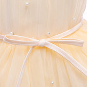 Close-up of a yellow dress with a white belt and pearl decorations.