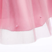 Close-up of a pink and white tulle skirt with pearl buttons on a light background