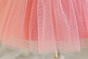 Close-up of a pink tulle skirt with small red polka dots on a plain background