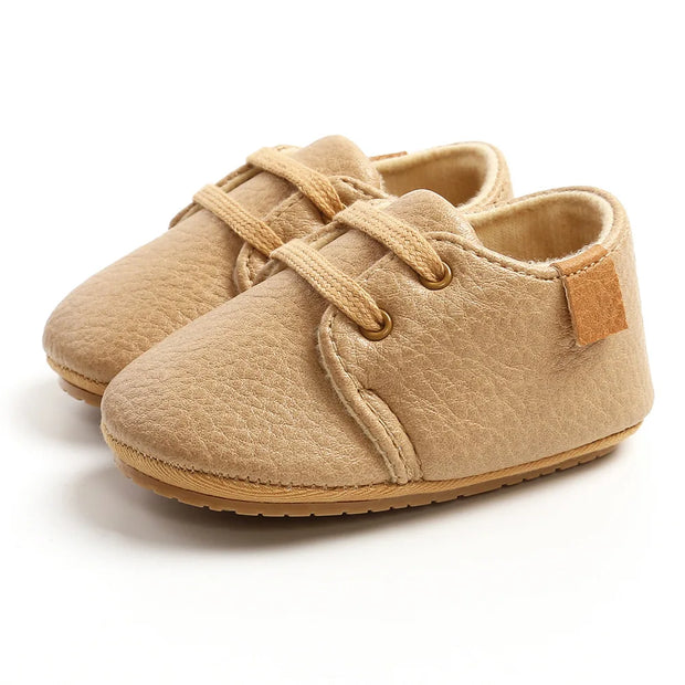 Pair of beige baby shoes with soft sole on a white background