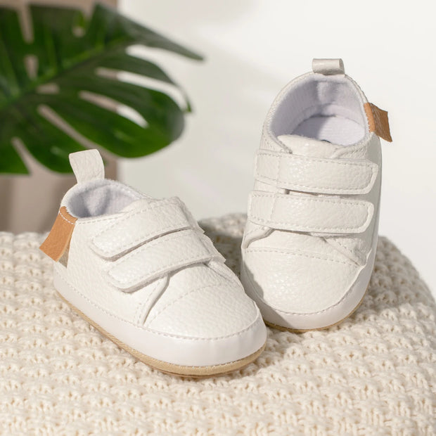 White baby shoes with velcro straps on a textured surface with a plant in the background