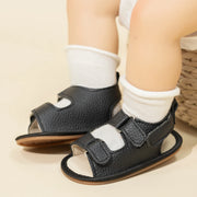 Black open-toe shoes with straps worn by a child on a beige background
