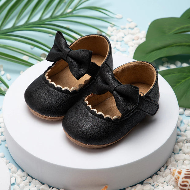 Black leather shoes with bows on a white platform with green leaves in the background