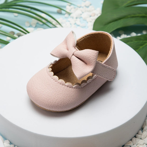 Pink baby shoe with a bow on a white platform with a natural background