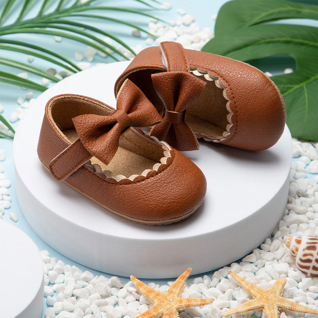 Pair of brown leather baby shoes with bows on a white platform with decorative elements.