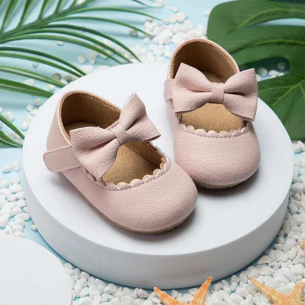 Pair of pink baby shoes with bows on a white platform with a natural background
