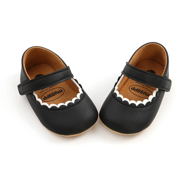 Pair of black baby shoes with a strap on a white background