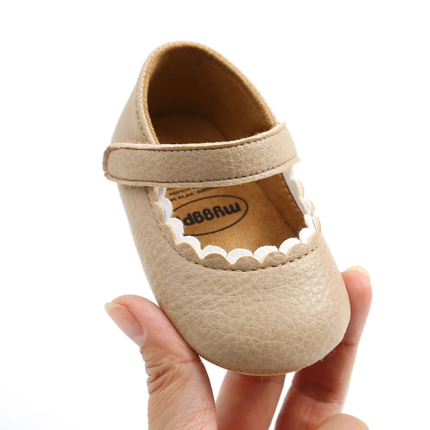 Beige baby shoe with a strap held by a hand on a white background