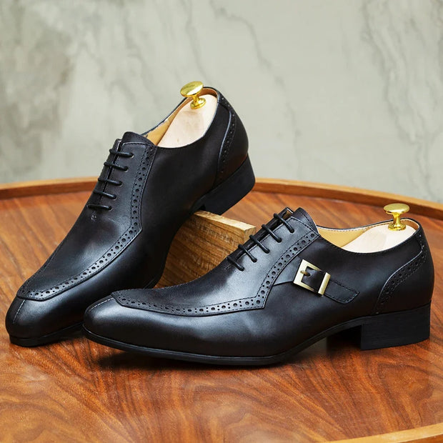 Pair of black leather dress shoes with a gold buckle on a wooden surface.
